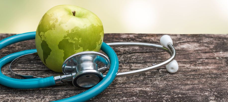 green apple with earth image overlay on table with blue stethoscope